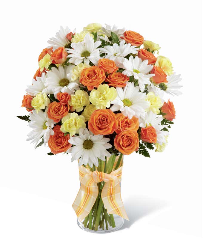 Tall and round arrangement of white daisies, yellow carns, and yellow roses in a cylinder vase