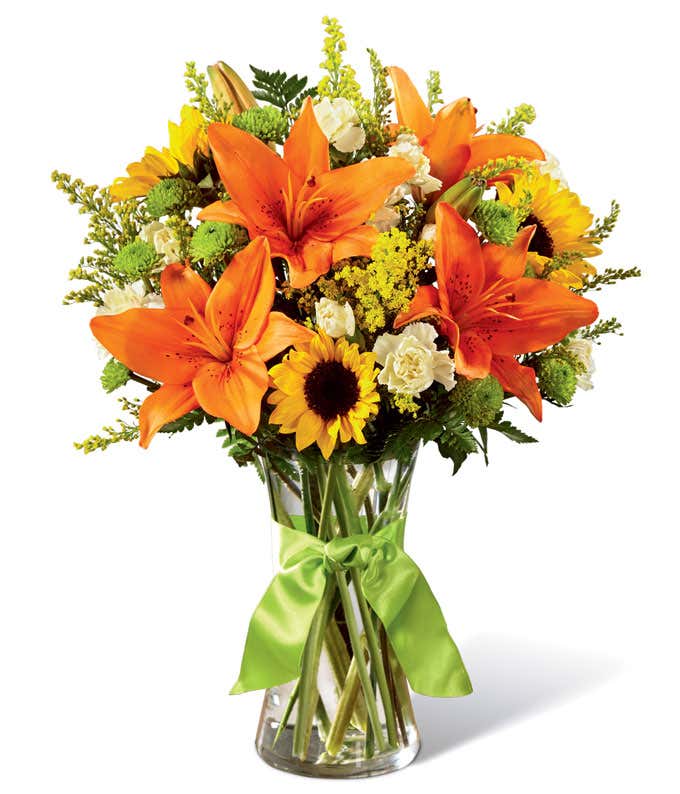 Tall arrangement of orange lilies, yellow sunflowers, with yellow and green accent flowers, in a tall cylinder vase