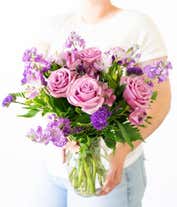 Alternative image 3 for A bouquet of lavender roses, purple alstroemeria and statice, with fresh floral greens, in a clear glass vase 