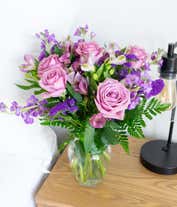 Alternative image 4 for A bouquet of lavender roses, purple alstroemeria and statice, with fresh floral greens, in a clear glass vase 