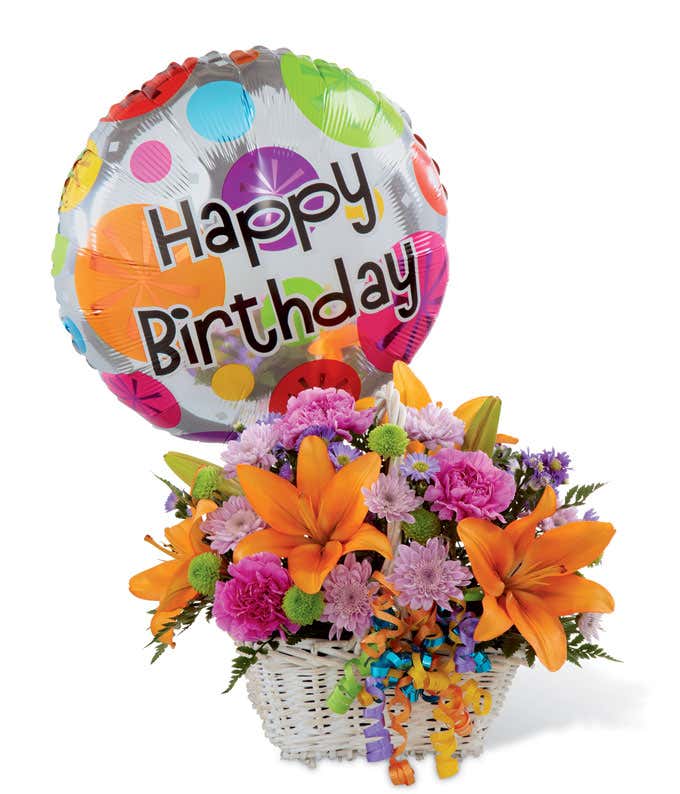 Orange lilies and purple and green flowers arranged into a white basket, with a happy birthday balloon and curling ribbon