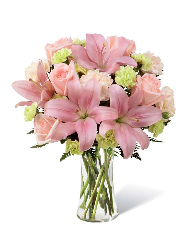 Light pink lilies and lilies, with pink and green carnations, in a tall cylinder vase