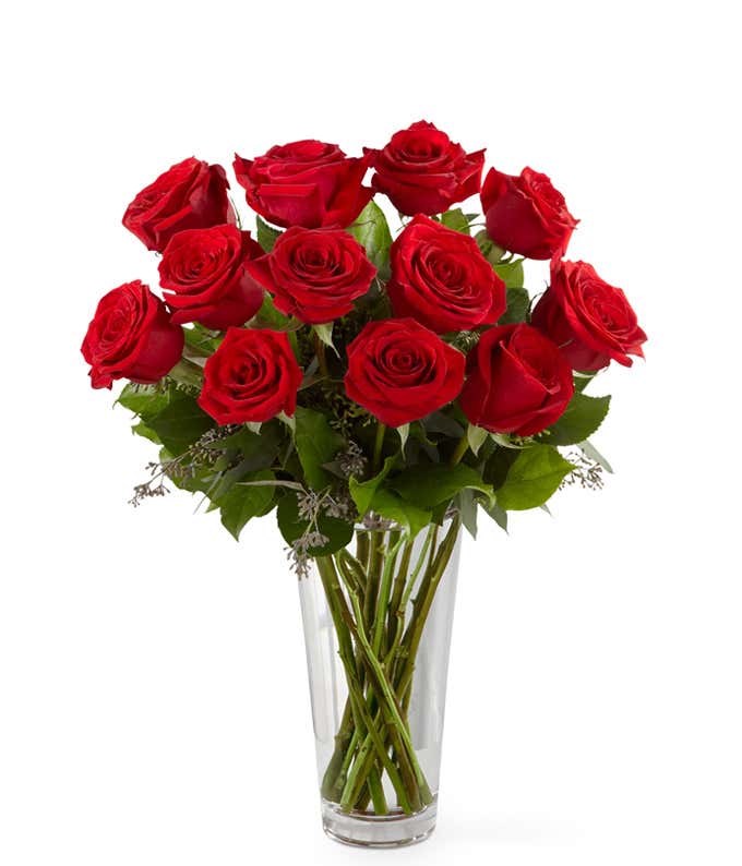 One dozen red roses with fresh floral greens in a clear glass vase