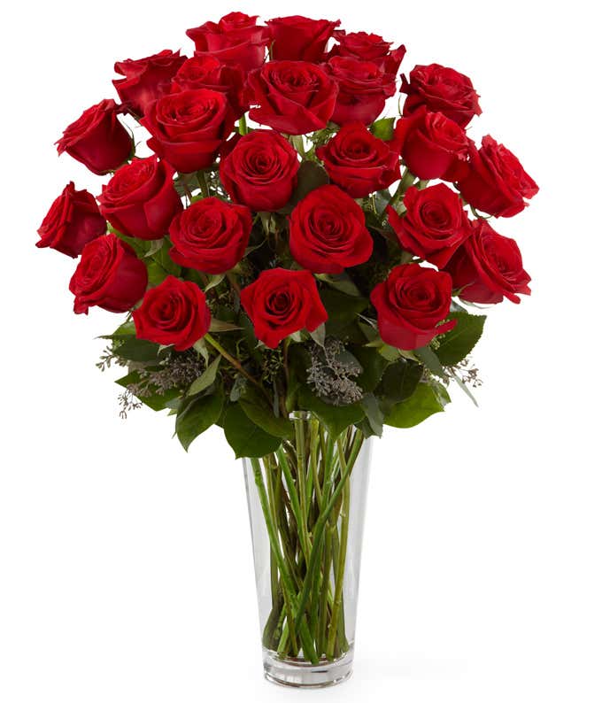 Two dozen red roses with fresh floral greens in a tall clear glass vase