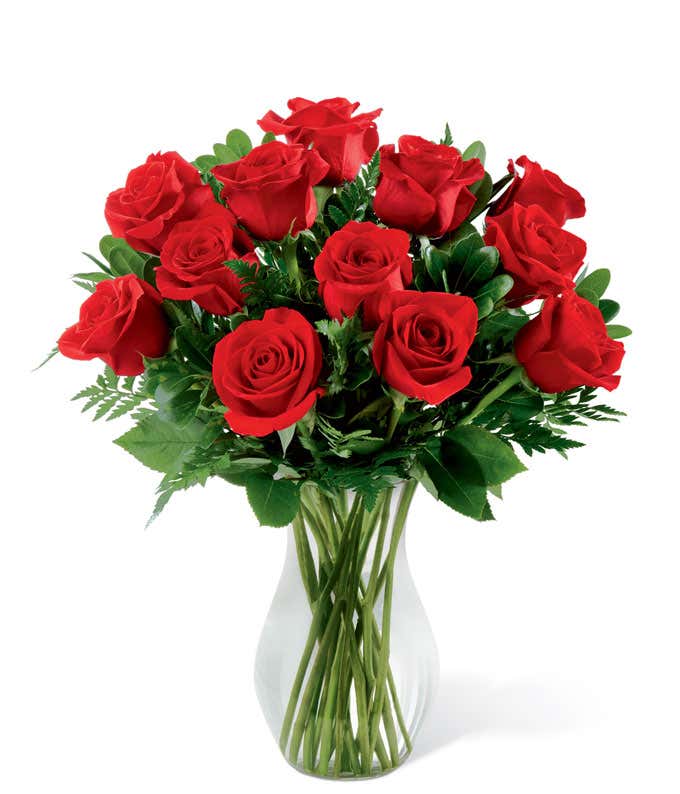 A dozen red roses with fresh floral greens in a tall cylinder vase