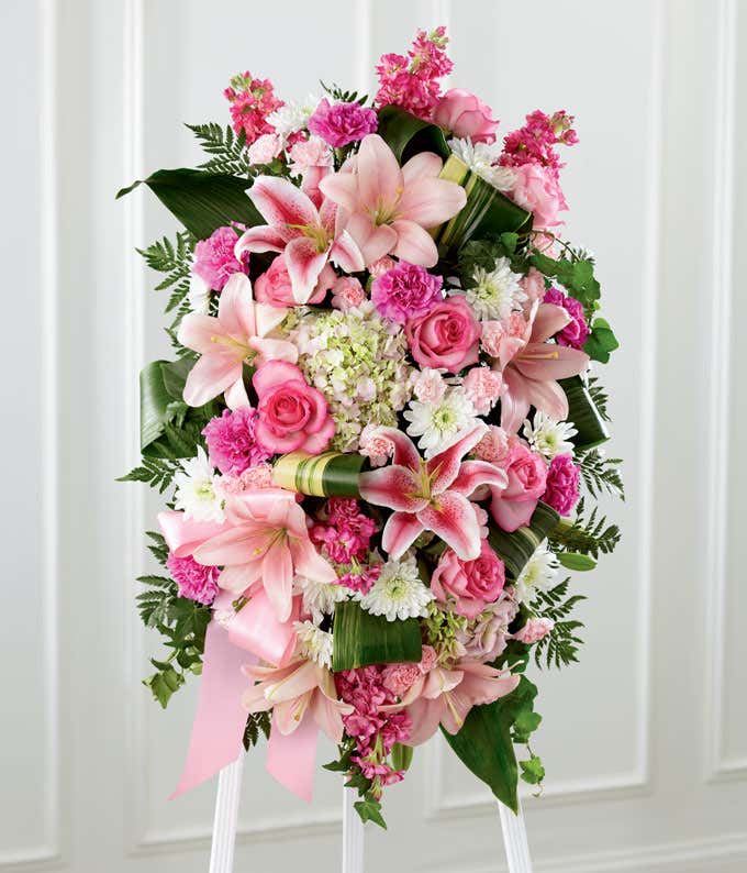 A standing spray of pink roses, lilies, hydrangea, and carnations, with white mums and fresh floral greens
