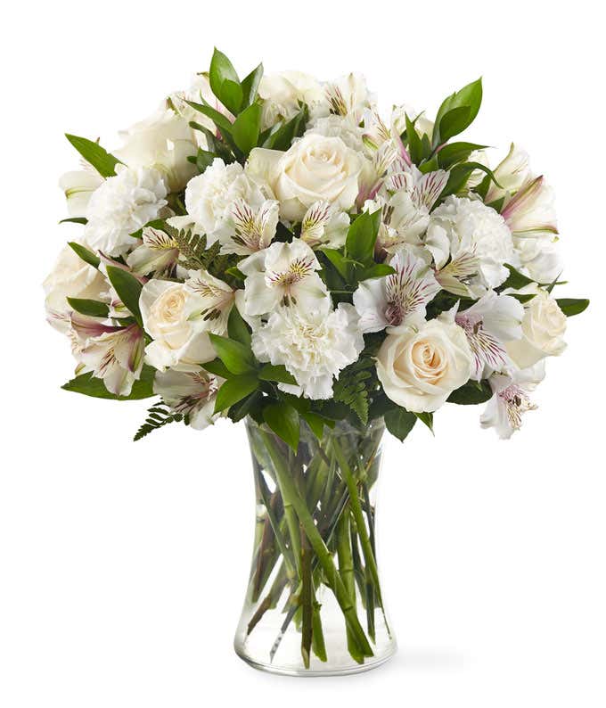 White roses, carnations, and alstroemeria, with mixed floral greens, in a tall cylinder vase