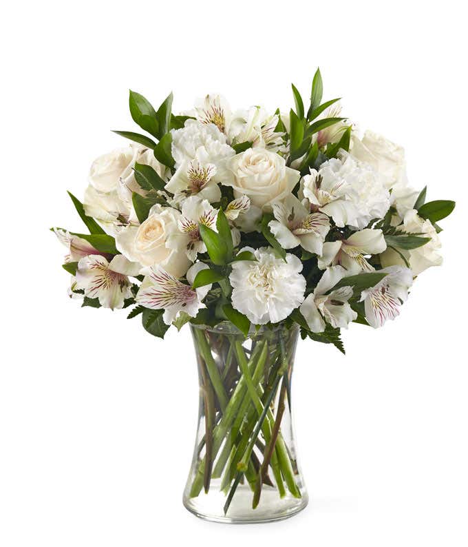 White roses, carnations, and alstroemeria, with mixed floral greens, in a tall cylinder vase