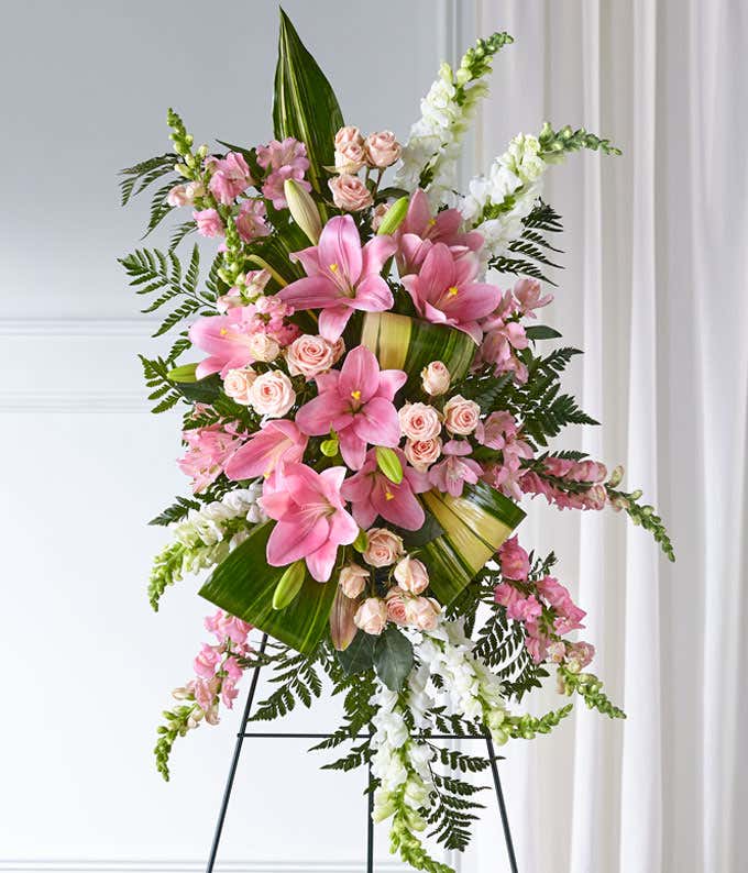 A standing spray of pink lilies, and roses with pink and white snapdragons, and fresh floral greens