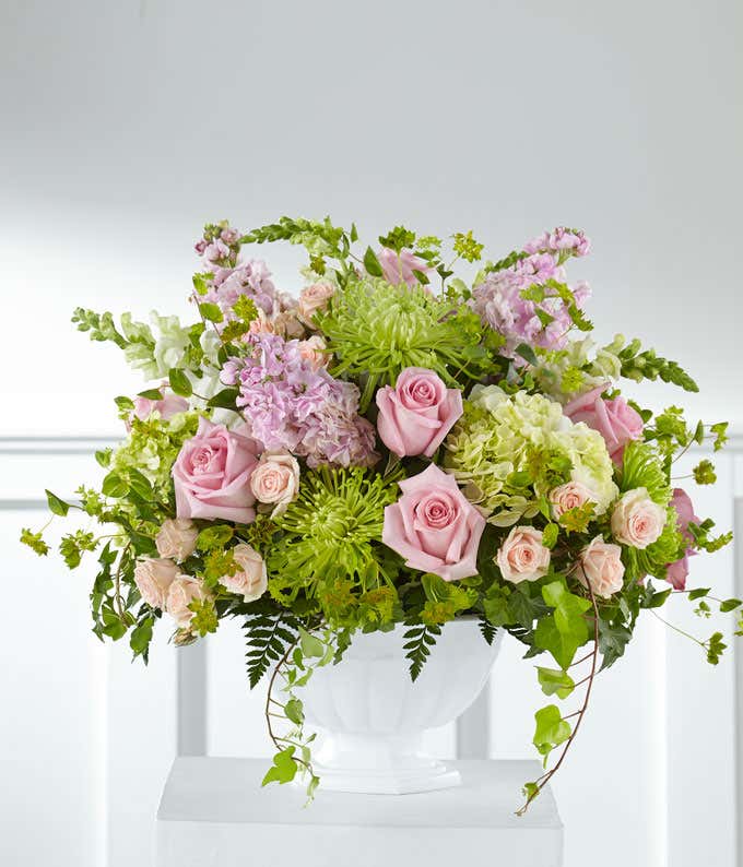 Standing basket of green hydrangeas, pink roses, and white snapdragons, in a white plastic urn