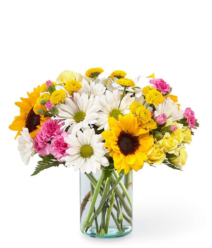 Sunflowers, white daisies, yellow spray roses, pink carnations, and fresh greens, arranged into a mason jar