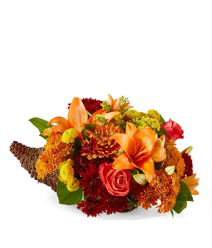 Orange Lilies & Roses, yellow, red, and butterscotch Poms, floral greens in a brown cornucopia against a white background