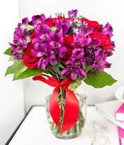 Alternative image 2 for A bouquet with red roses, purple alstroemeria, and purple daisy poms in a clear vase tied with a red ribbon.