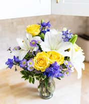 Alternative image 1 for Yellow roses, blue delphinium and white lilies in a vase for Mothers Day