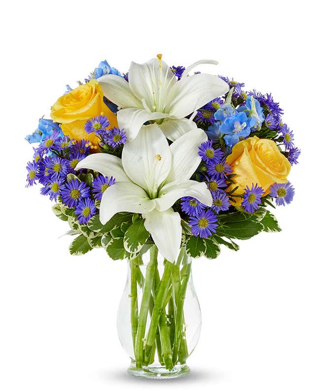 Yellow roses, blue delphinium and white lilies in a vase for Mothers Day