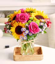 Alternative image 1 for Floral arrangement featuring sunflowers, red alstroemeria, pink roses (in deluxe and premium versions), purple monte casino, and green button poms in a mason jar vase, with a personalized card message.