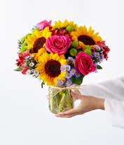 Alternative image 4 for Floral arrangement featuring sunflowers, red alstroemeria, pink roses (in deluxe and premium versions), purple monte casino, and green button poms in a mason jar vase, with a personalized card message.