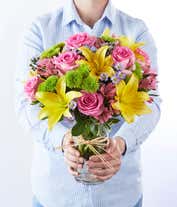 Alternative image 3 for A vibrant arrangement featuring yellow lilies, pink roses, pink alstroemeria, green poms, and purple Monte Casino, beautifully arranged in a glass vase. This colorful mix offers a cheerful and eye-catching display, perfect for brightening any occasion.