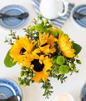 Alternative image 2 for  A bright floral arrangement featuring sunflowers and green hypericum, elegantly displayed in a clear cube vase.