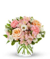 A delightful floral arrangement of peach roses, pink carnations, pink alstroemeria, and white lisianthus, elegantly arranged in a glass vase. This soft and romantic mix of flowers offers a gentle and inviting display.