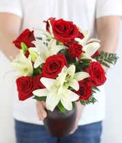 Alternative image 2 for A floral arrangement featuring red roses and white lilies in a red cylinder vase.