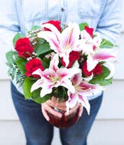 Alternative image 2 for A striking arrangement featuring red roses, stargazer lilies, waxflower, and seasonal greens, elegantly presented in a red cylinder vase. This bold and vibrant display is perfect for adding a touch of elegance and passion to any occasion.