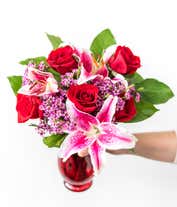 Alternative image 3 for A striking arrangement featuring red roses, stargazer lilies, waxflower, and seasonal greens, elegantly presented in a red cylinder vase. This bold and vibrant display is perfect for adding a touch of elegance and passion to any occasion.