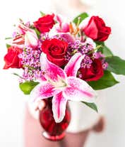 Alternative image 4 for A striking arrangement featuring red roses, stargazer lilies, waxflower, and seasonal greens, elegantly presented in a red cylinder vase. This bold and vibrant display is perfect for adding a touch of elegance and passion to any occasion.