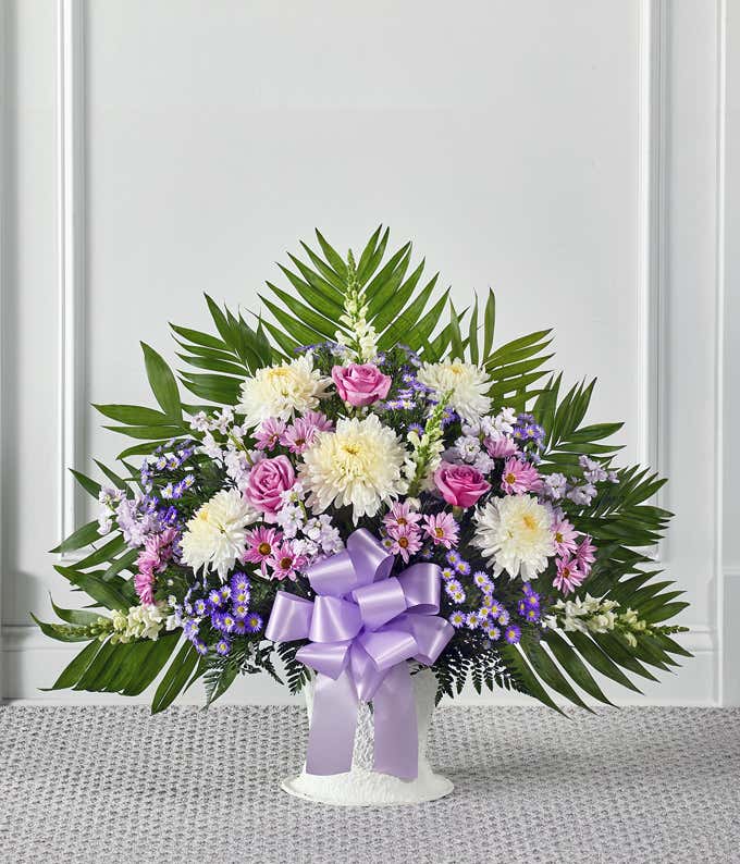 A heartfelt sympathy floor basket featuring white roses, white snapdragons, lavender stock, lavender mums, and white Monte Casino. This elegant and serene arrangement offers a comforting and respectful tribute. 