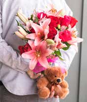 Alternative image 3 for A romantic arrangement featuring red and pink roses, pink lilies, purple waxflowers, and alstroemeria, beautifully arranged in a clear vase with a bow. Includes a keepsake teddy bear and a box of chocolate for an extra touch of love.