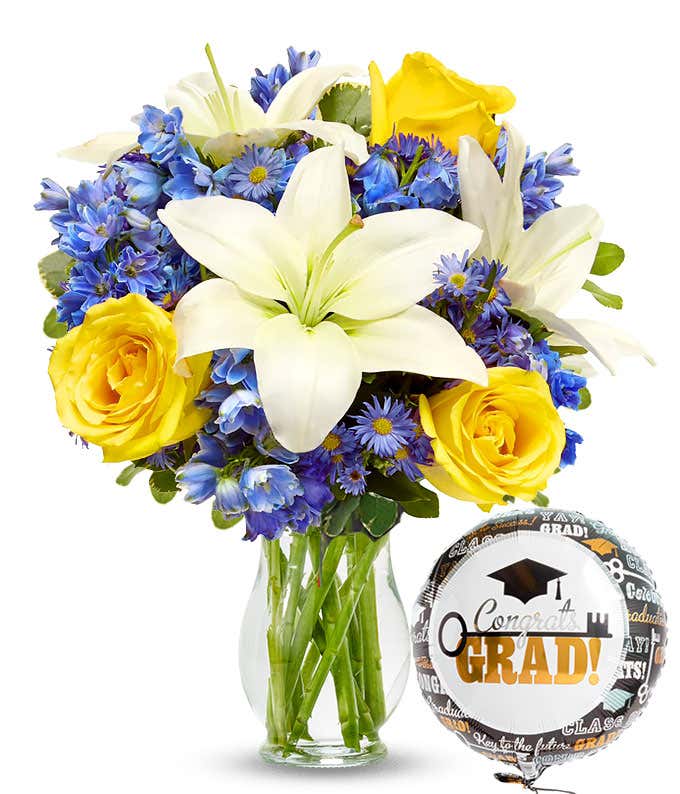 bouquet of yellow roses, white lilies, blue and purple flowers in a clear glass vase with a graduation balloon.