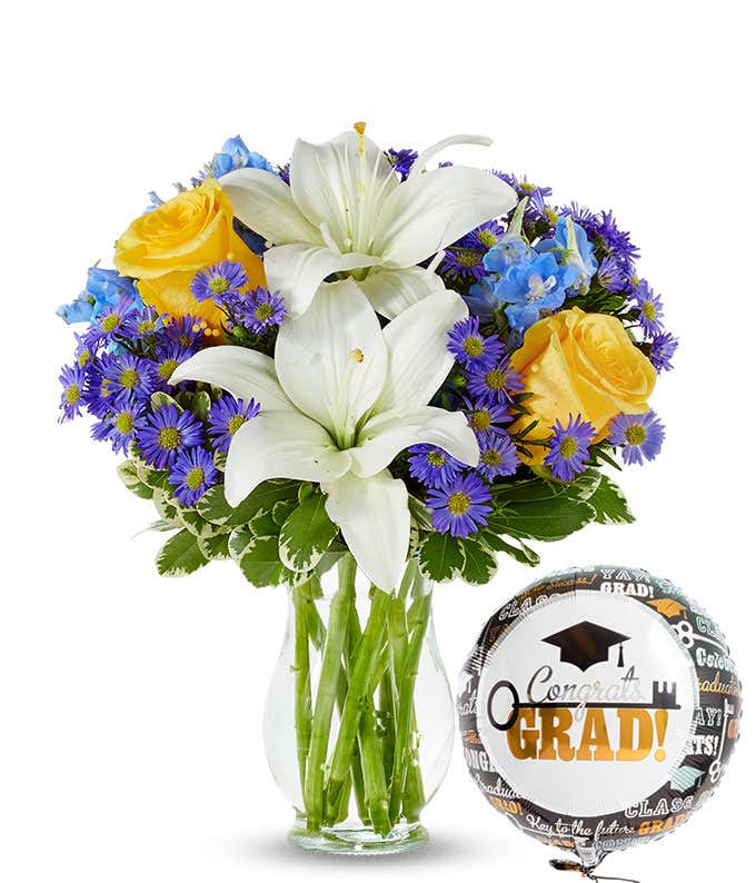 bouquet of yellow roses, white lilies, blue and purple flowers in a clear glass vase with a graduation balloon.