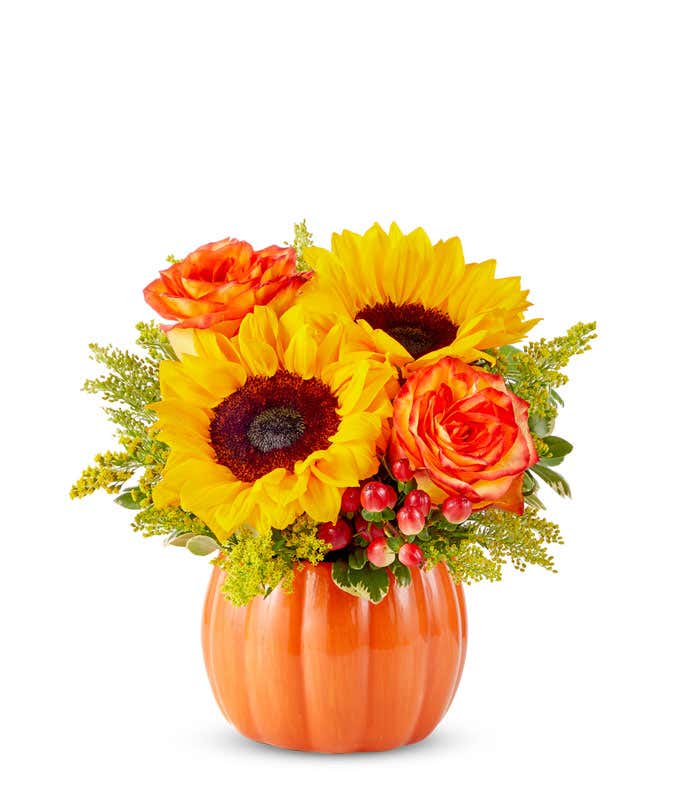  A cheerful floral arrangement featuring sunflowers, orange roses, safari sunset, red berries, and yellow solidago, all beautifully arranged in a pumpkin container.