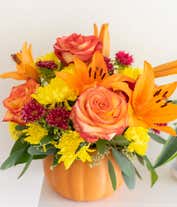 Alternative image 1 for  A cheerful floral arrangement featuring orange roses, orange lilies, red Matsumoto asters, and yellow poms, all beautifully arranged in a pumpkin ceramic container.