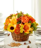 Alternative image 1 for A vibrant floral arrangement featuring yellow Asiatic lilies, deluxe size orange roses, regular size orange carnations, yellow button poms, bronze cushion poms, red hypericum, and solidago, all beautifully presented in a basket.