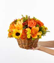 Alternative image 2 for A vibrant floral arrangement featuring yellow Asiatic lilies, deluxe size orange roses, regular size orange carnations, yellow button poms, bronze cushion poms, red hypericum, and solidago, all beautifully presented in a basket.