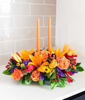 Alternative image 1 for Fall centerpiece with orange candles, orange lilies, roses, yellow poms, purple statice, and red hypericum berries.