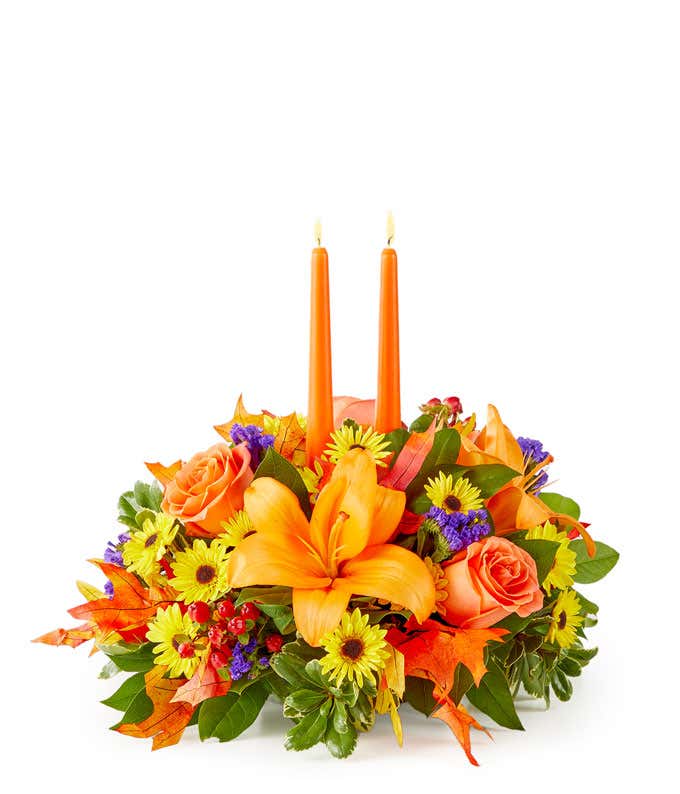 Fall centerpiece with orange candles, orange lilies, roses, yellow poms, purple statice, and red hypericum berries.