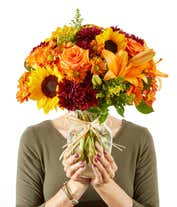 Alternative image 2 for A vibrant fall bouquet in clear glass vase, sunflowers and orange lilies and roses are surrounded by yellow and maroon filler flowers in a clear glass vase.