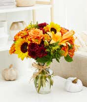 Alternative image 3 for A vibrant fall bouquet in clear glass vase, sunflowers and orange lilies and roses are surrounded by yellow and maroon filler flowers in a clear glass vase.