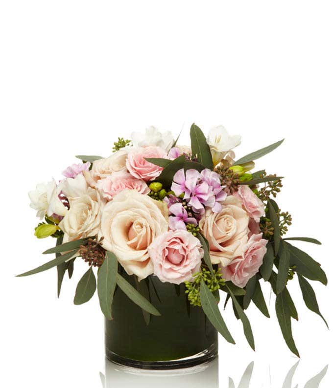 Champagne roses arranged in cylinder vase with light pink roses and white freesia