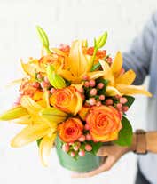 Alternative image 1 for A beautiful floral arrangement featuring orange roses, peach roses, and coral hypericum, all elegantly presented in a round glass vase.