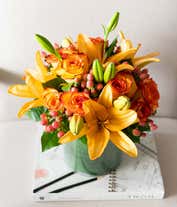 Alternative image 2 for A beautiful floral arrangement featuring orange roses, peach roses, and coral hypericum, all elegantly presented in a round glass vase.