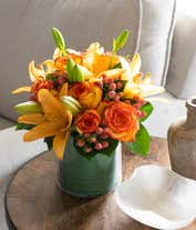 Alternative image 3 for A beautiful floral arrangement featuring orange roses, peach roses, and coral hypericum, all elegantly presented in a round glass vase.