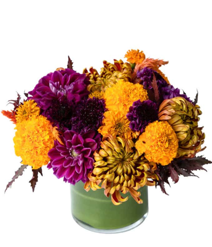 Premium flowers in colors of orange, purple, and bronze arranged in a leaf lined vase.