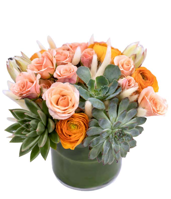 Short arrangement of pink, orange, and creme colors, with a succulent, in a leaf-lined vase