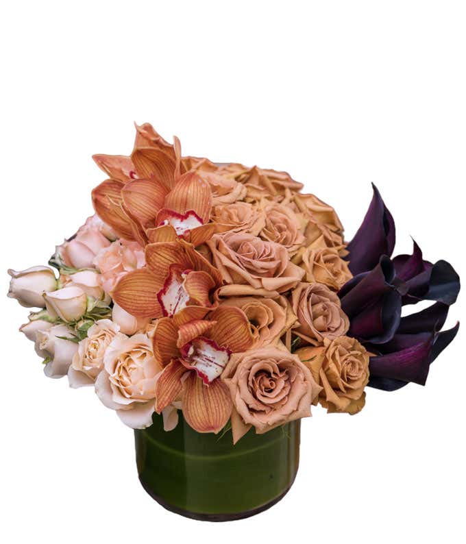 Flowers in colors of cream, brown, and burgundy arranged into a short leaf-lined cylinder vase