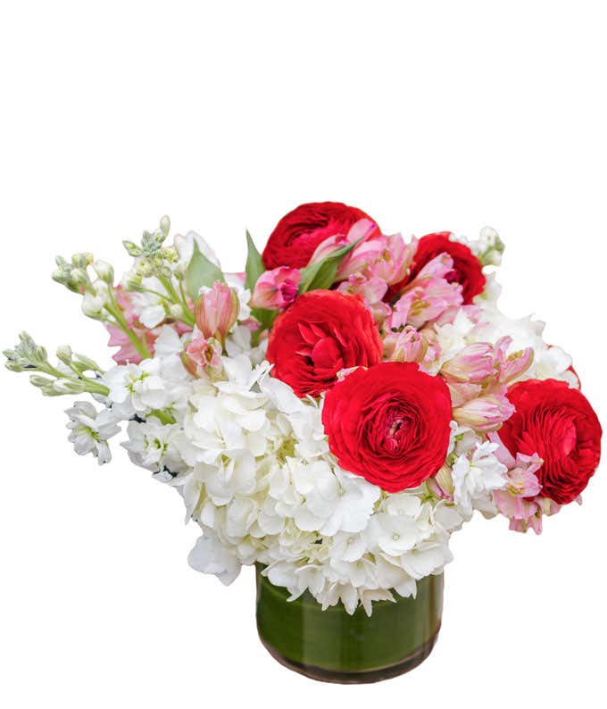 Short arrangement of white, red, and pink flowers in a leaf-lined cylinder vase