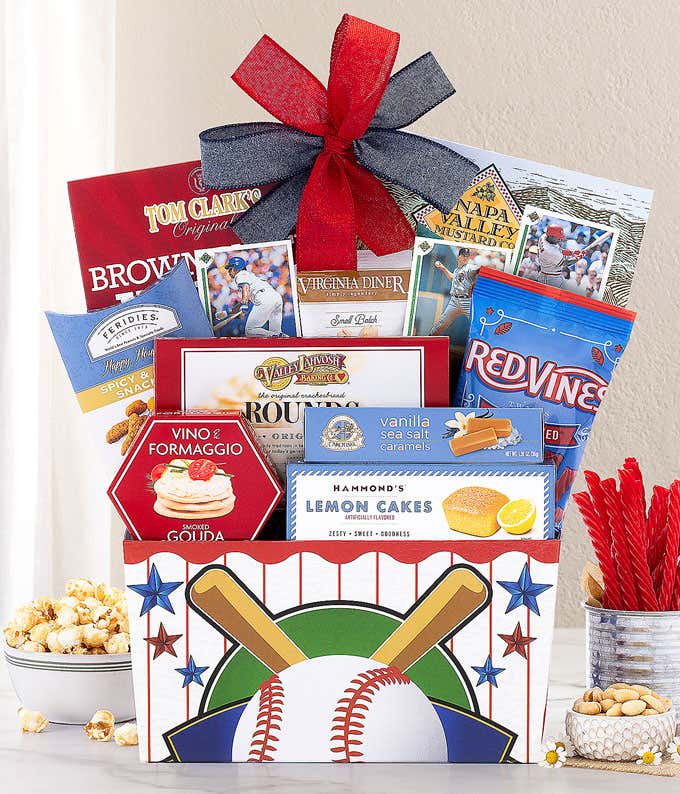 This baseball-themed gift basket, topped with a red and blue bow, includes Red Vines, Hammond's Lemon Cakes, Gouda, Lahvosh crackers, Spicy Hot Peanuts, Tom Clark's Caramel Popcorn, and Napa Valley Mustard, all with a fun baseball motif