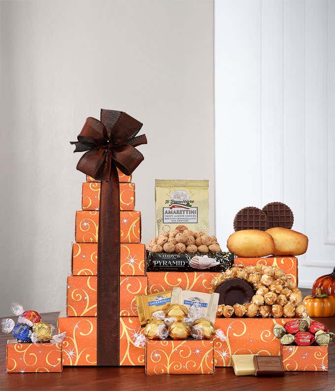 Thanksgiving gift tower with festive orange boxes filled with chocolates, cookies, and snacks, topped with a gold bow and a 